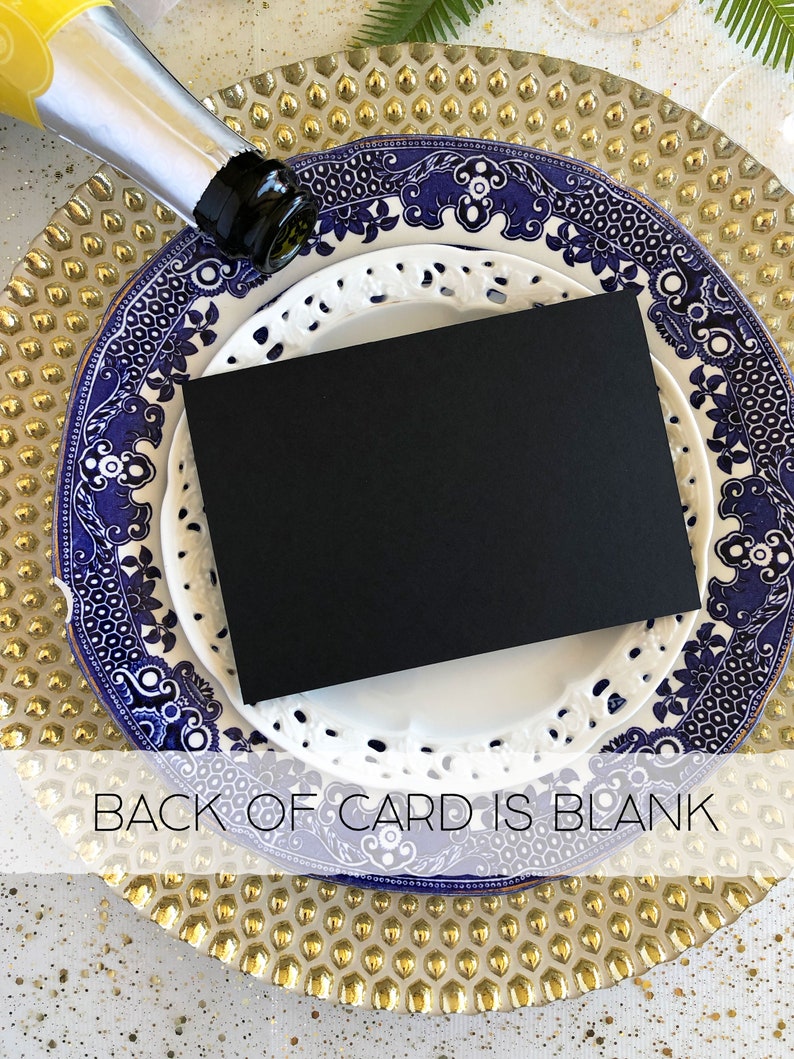 Pode incluir: Um cart&atilde;o preto com uma borda branca est&aacute; sobre um prato com um padr&atilde;o azul e branco. O prato est&aacute; sobre um prato de carga dourado. O texto "BACK OF CARD IS BLANK" &eacute; vis&iacute;vel na parte inferior da imagem.