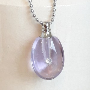 May include: A silver chain necklace with a clear, faceted, lavender glass pendant. The pendant has a small, clear rhinestone in the center.