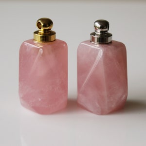 May include: Two pink rose quartz bottles with gold and silver lids. The bottles are square shaped and have a faceted design.