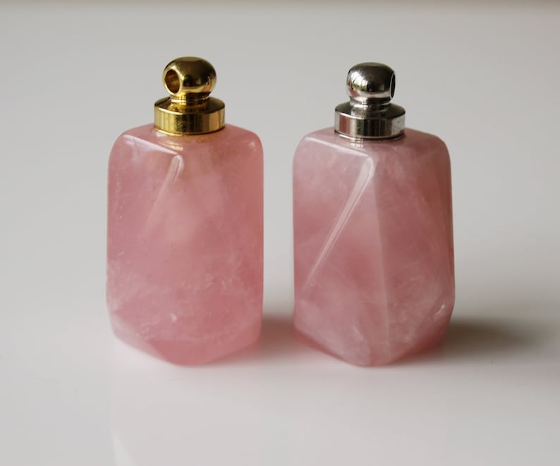 May include: Two pink rose quartz bottles with gold and silver lids. The bottles are square shaped and have a faceted design.