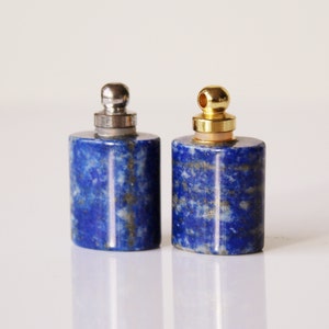 May include: Two small, cylindrical, blue lapis lazuli bottles with gold and silver caps. The bottles are made of natural stone and have a speckled appearance.