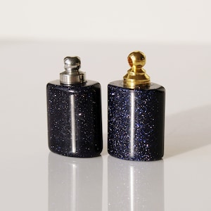 May include: Two small, dark blue glass bottles with silver and gold tops. The bottles have a sparkly, glittery finish.