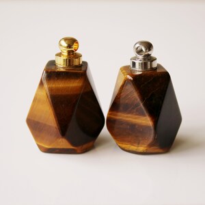 May include: Two geometric tiger's eye stone bottles with gold and silver caps. The bottles are faceted and have a brown and gold color.