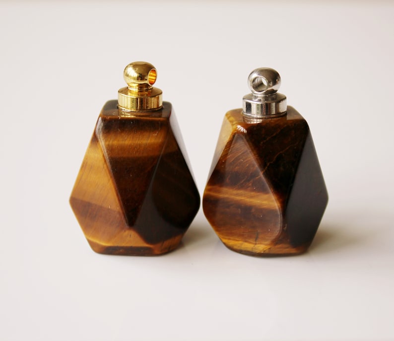 May include: Two geometric tiger's eye stone bottles with gold and silver caps. The bottles are faceted and have a brown and gold color.
