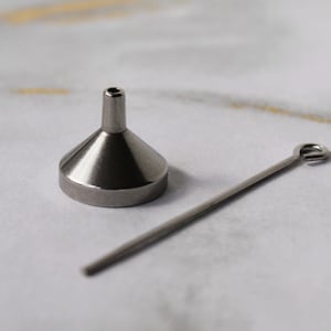 May include: A small, silver funnel with a long, thin, silver rod with a loop at one end. The funnel and rod are on a white surface.