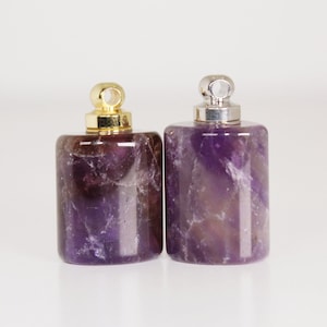 May include: Two amethyst stone bottle stoppers with gold and silver caps. The stoppers are rectangular in shape and have a purple hue.