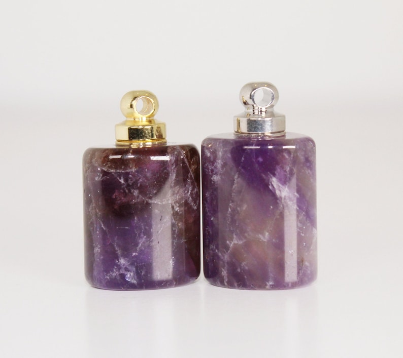 May include: Two amethyst stone bottle stoppers with gold and silver caps. The stoppers are rectangular in shape and have a purple hue.
