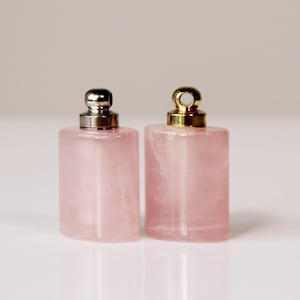 May include: Two small pink rose quartz bottles with silver and gold metal caps. The bottles are rectangular with rounded edges.