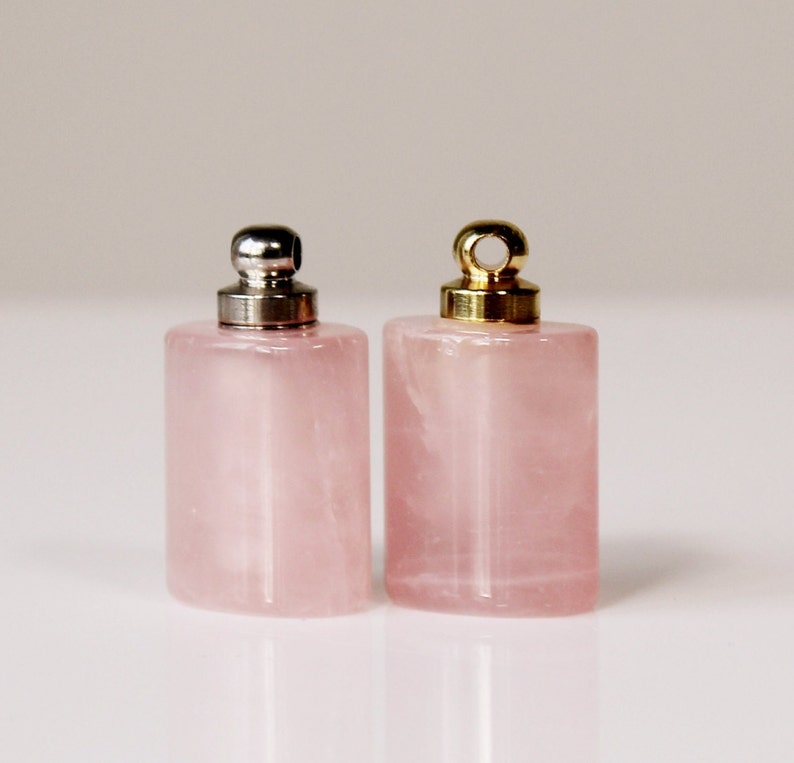 May include: Two small pink rose quartz bottles with silver and gold metal caps. The bottles are rectangular with rounded edges.