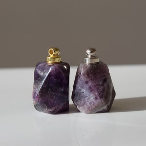 May include: Two small amethyst crystal bottles with gold and silver stoppers. The bottles are faceted and have a purple hue.