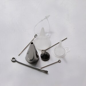 May include: A set of four funnels, including two clear plastic funnels, one silver metal funnel, and one small silver metal funnel with a cap. The funnels are arranged on a white surface with a silver metal wire.