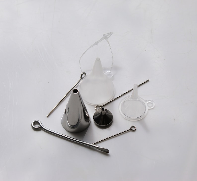 May include: A set of four funnels, including two clear plastic funnels, one silver metal funnel, and one small silver metal funnel with a cap. The funnels are arranged on a white surface with a silver metal wire.