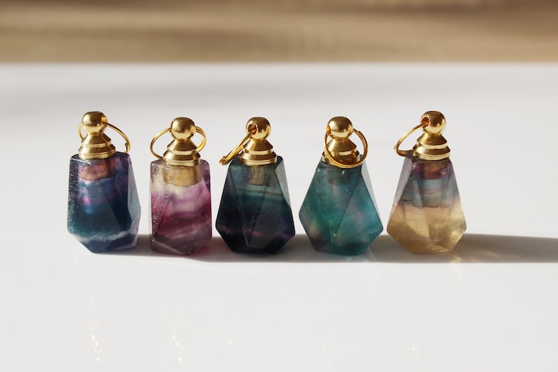 May include: Five small, faceted, gemstone bottles with gold stoppers. The bottles are in shades of green, blue, purple, and yellow.