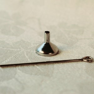 May include: A small silver funnel with a long, thin silver rod.