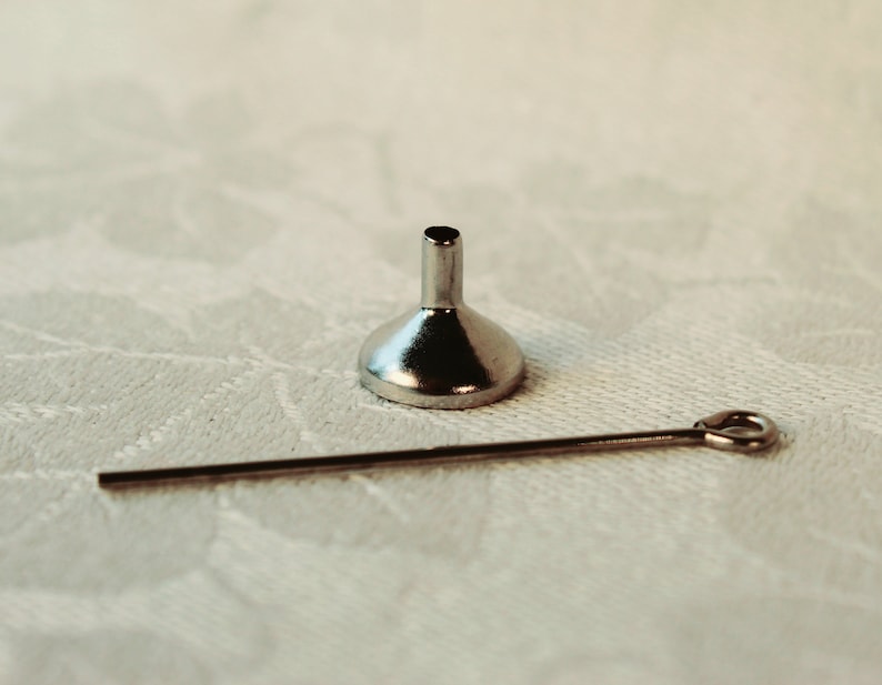 May include: A small silver funnel with a long, thin silver rod.