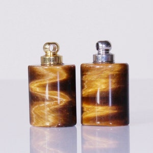 May include: Two small, cylindrical, tiger's eye stone bottles with gold and silver caps. The bottles have a brown and gold color with a swirling pattern.