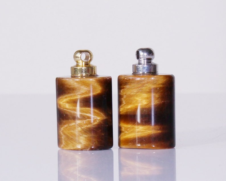 May include: Two small, cylindrical, tiger's eye stone bottles with gold and silver caps. The bottles have a brown and gold color with a swirling pattern.