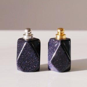 May include: Two small, dark blue glass bottles with gold and silver lids. The bottles have a geometric, faceted design and a sparkly finish.