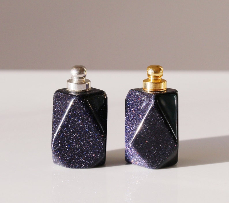 May include: Two small, dark blue glass bottles with gold and silver lids. The bottles have a geometric, faceted design and a sparkly finish.