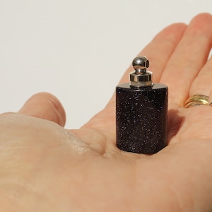 May include: A small, dark blue glass bottle with a silver top and a silver ball on top. The bottle is filled with a dark blue liquid.