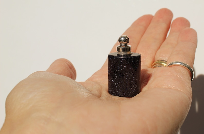 May include: A small, dark blue glass bottle with a silver top and a silver ball on top. The bottle is filled with a dark blue liquid.