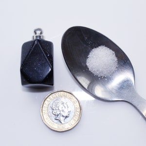 May include: A small, dark blue, faceted glass bottle with a silver lid, a spoon with a pile of white powder, and a British one pound coin.