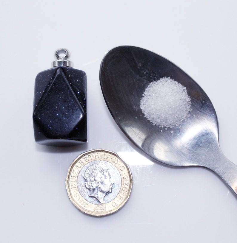 May include: A small, dark blue, faceted glass bottle with a silver lid, a spoon with a pile of white powder, and a British one pound coin.