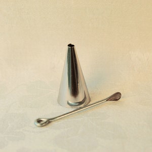 May include: A silver metal piping tip with a round opening and a long, thin, silver metal tool with a rounded end.