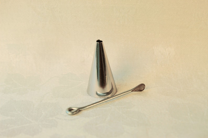May include: A silver metal piping tip with a round opening and a long, thin, silver metal tool with a rounded end.