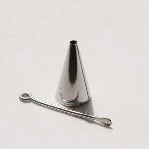 May include: A silver metal piping tip with a round opening and a small metal tool with a loop at one end.