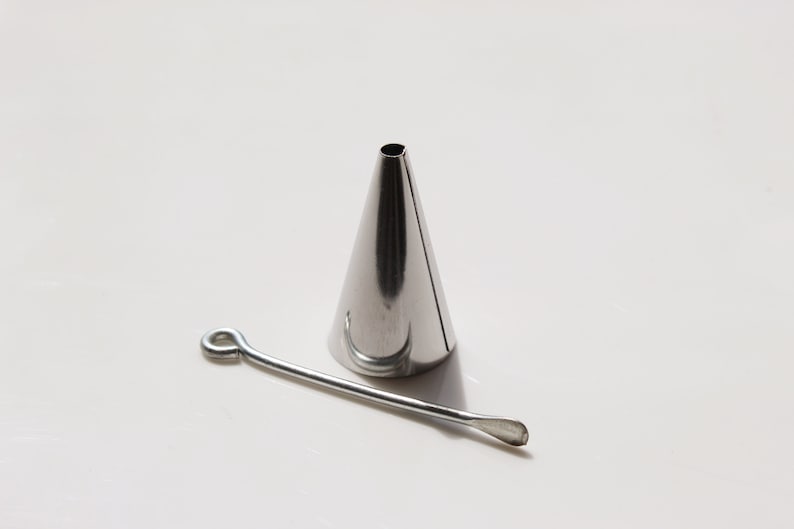 May include: A silver metal piping tip with a round opening and a small metal tool with a loop at one end.