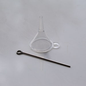 May include: A clear plastic funnel with a small metal hook and a thin metal rod with a loop at one end.