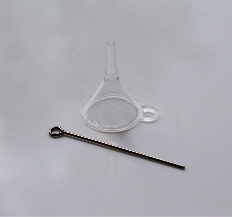 May include: A clear plastic funnel with a small metal hook and a thin metal rod with a loop at one end.