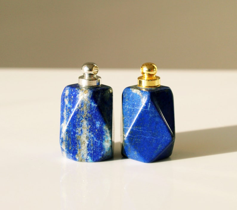 May include: Two small, geometrically shaped bottles made of blue lapis lazuli stone with silver and gold caps.