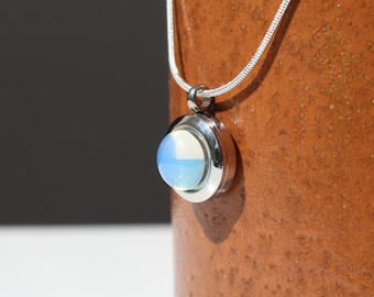 Peut inclure: Un collier en chaîne argent avec un pendentif rond orné d'une opale bleue et blanche.