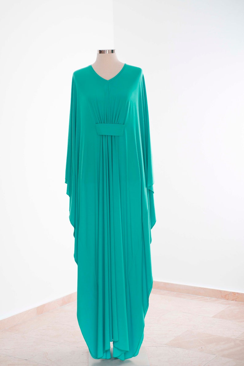 May include: A flowing, turquoise-colored caftan dress with a V-neck and wide sleeves. The dress is displayed on a mannequin against a white background. The fabric is gathered at the waist with a horizontal band.