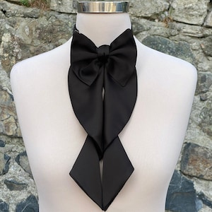 May include: A black satin bow tie with a long, flowing design. The bow tie is tied around a white mannequin's neck.