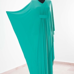 May include: A teal-colored, flowing kaftan dress displayed on a black mannequin. The dress features a V-neckline and a gathered detail at the waist. The fabric drapes elegantly, showcasing its loose, comfortable design. The dress is made of a soft, lightweight material.