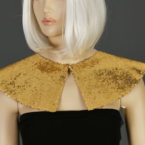 May include: A gold sequined collar with a pointed, rounded shape. The collar is made of small, shimmering sequins and has a simple, elegant design.