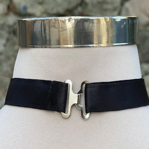 May include: A black satin choker with a silver clasp. The choker is on a white mannequin.
