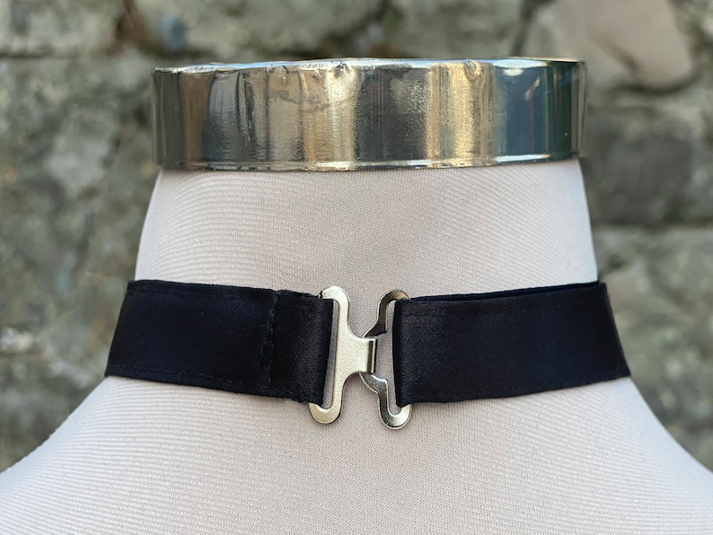 May include: A black satin choker with a silver clasp. The choker is on a white mannequin.
