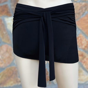 Puede incluir: Falda envolvente negra con cierre de lazo. La falda está hecha de una tela suave y fluida y está diseñada para usarse en la cintura. El detalle del lazo añade un toque elegante. Ideal para trajes de baño o ropa casual.