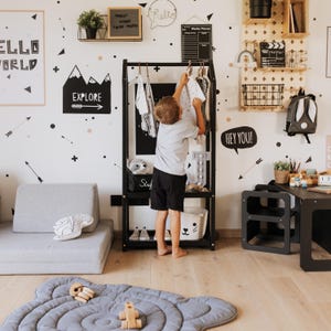 Young boy learning to tidy up his room using an accessible black clothes rack