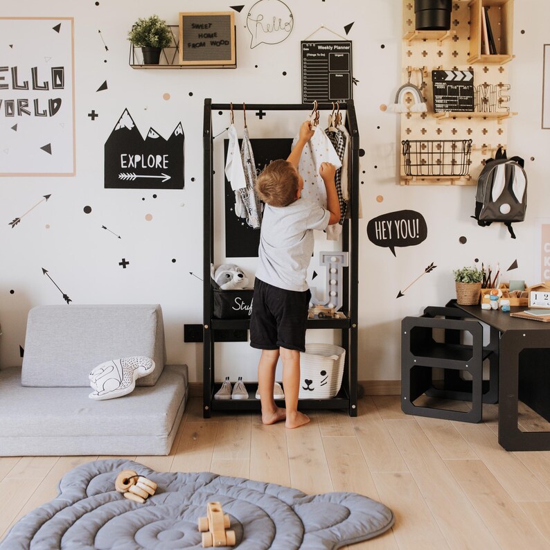 Young boy learning to tidy up his room using an accessible black clothes rack