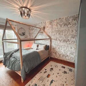 Natural wood cottage bed frame on legs styled in an adventurous woodland animal wallpaper nursery with ceiling chandelier.
