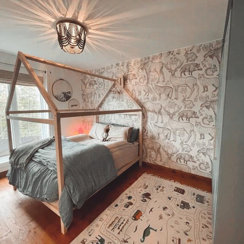 Natural wood cottage bed frame on legs styled in an adventurous woodland animal wallpaper nursery with ceiling chandelier.