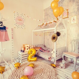 Natural solid wood canopy bed frame decorated with party balloons in a cozy kids playroom corner.