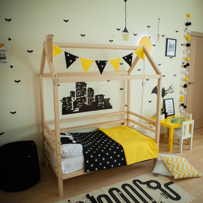 Natural solid wood house bed frame on legs with removable safety rails in a decorated toddler room.