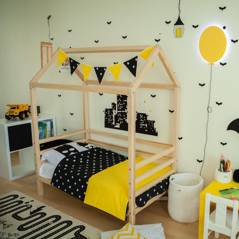 Natural solid wood toddler house bed frame with birch plywood slats and yellow bedding set up in a decorated child room.