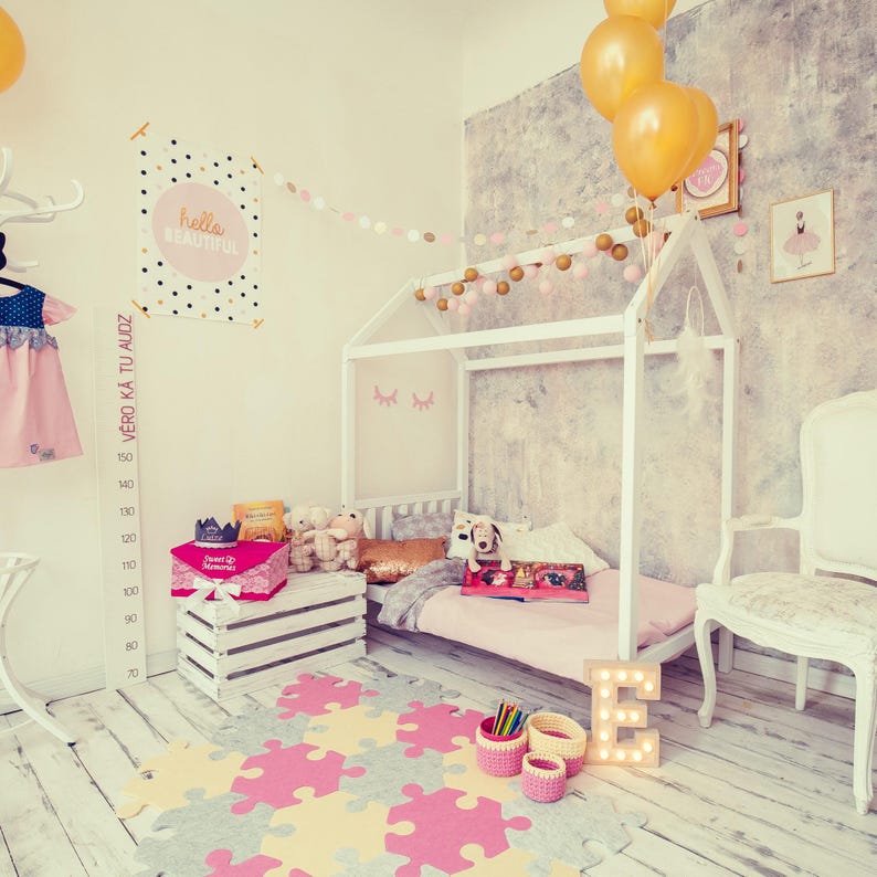 White house bed frame on legs in a festive party-styled nursery decorated with yellow balloons and soft pink bedding.